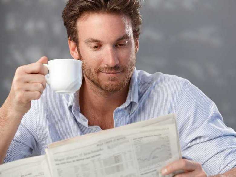 Mężczyzna przeglądający gazetę i popijający kawę